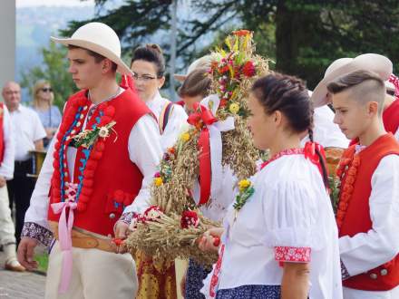 Ludzie w strojach regionalnych z koroną dożynkową