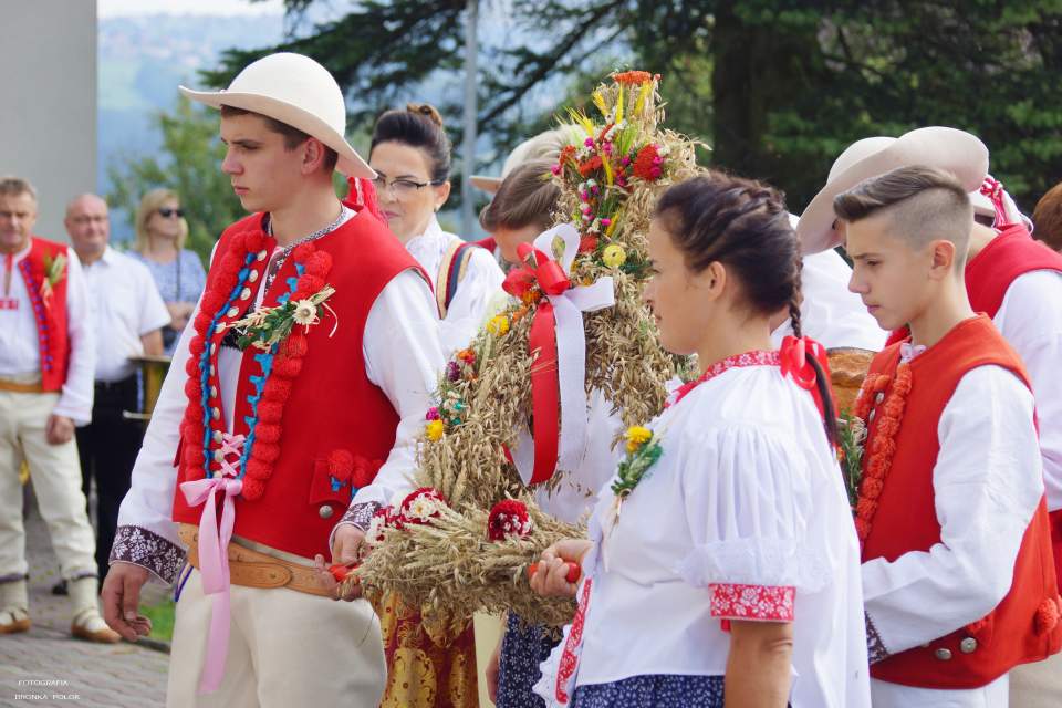 Ludzie w strojach regionalnych z koroną dożynkową